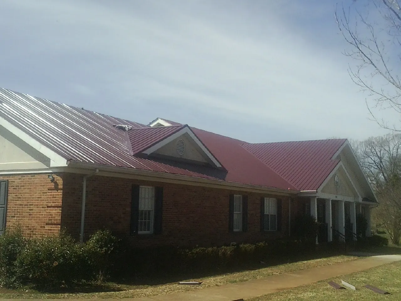 Red metal roof with gabled entries on a long brick building, from a Hail Damage Roof Repair job in Herminie