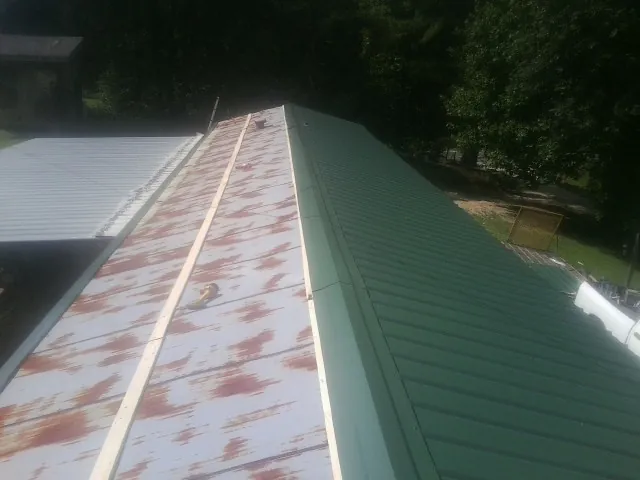 Old rusted panels beside newly installed green metal roofing — Wind Damage Roof Repair by Roofing Brothers in Herminie