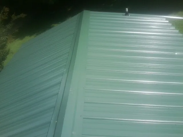 New green metal panels meeting at the ridge of a roof — Flat Roof Repair work by our crew in Herminie