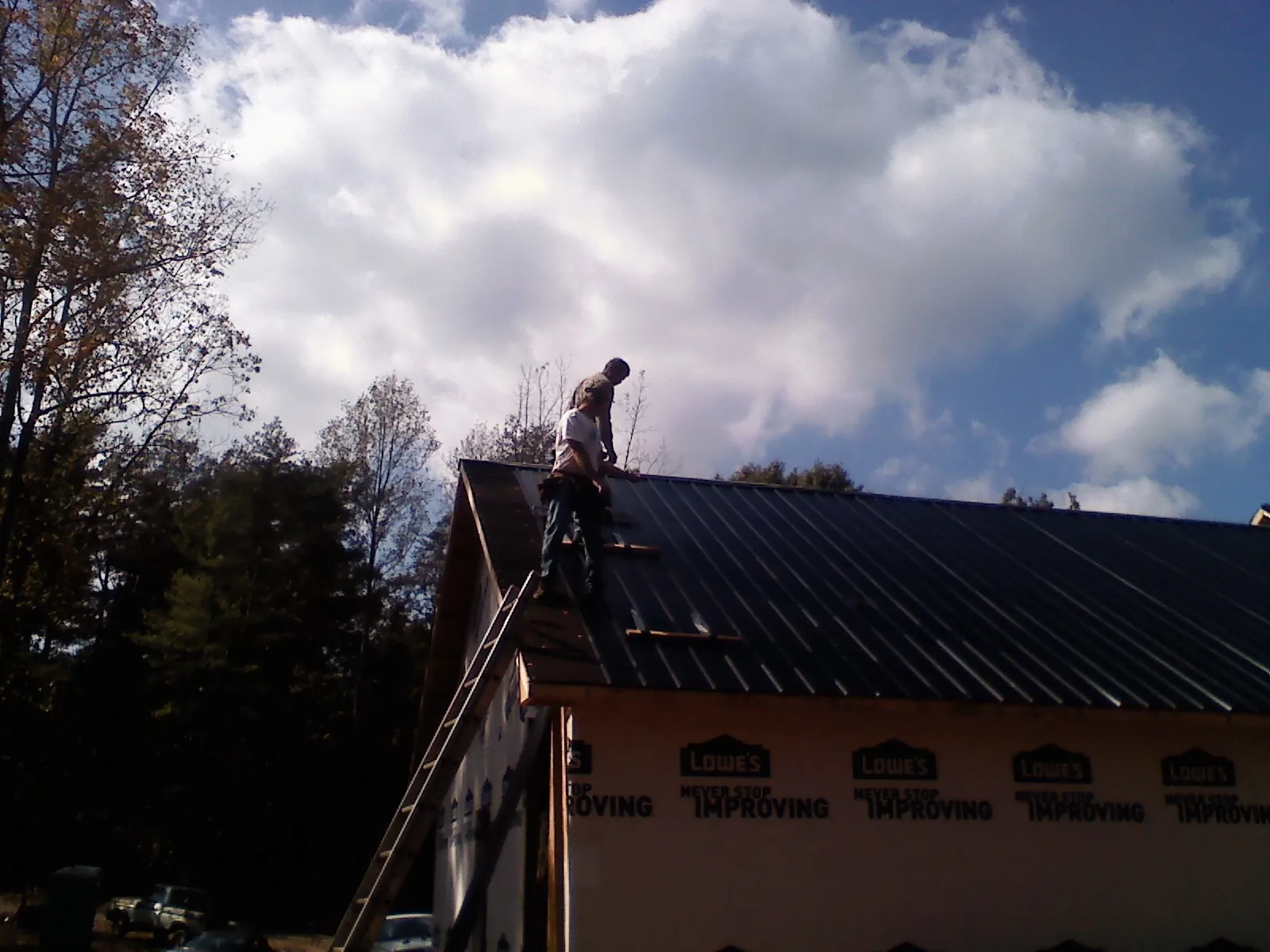 Roofer fastening dark metal panels high against a cloudy sky, from a Roof Inspection job in Herminie
