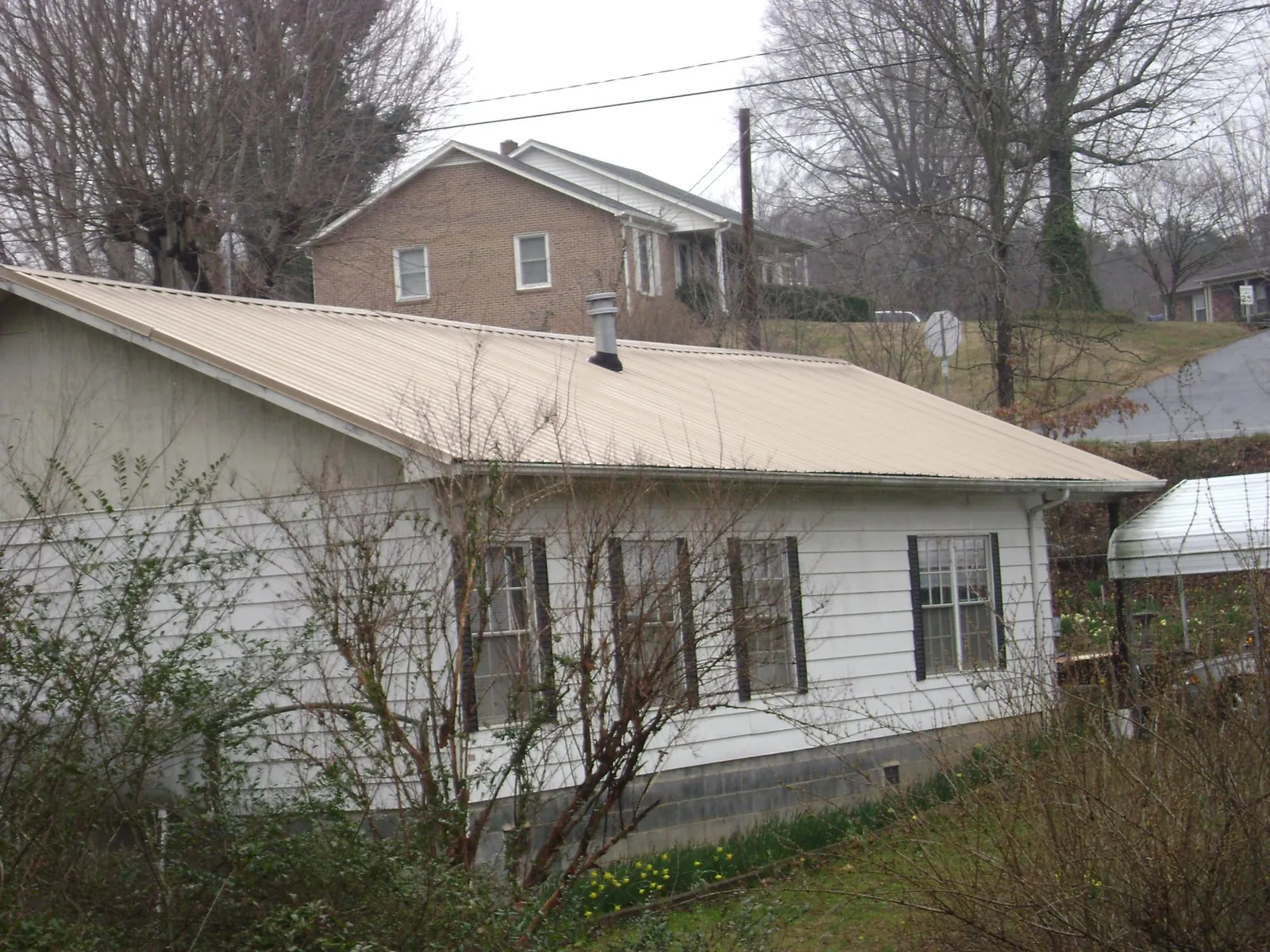 Tan metal roof on a white sided house set into a hillside — Commercial Roofing by Roofing Brothers in Herminie